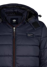 Marineblauwe pufferjack met hoge kraag, ritssluiting en geprint logo. Beschikt over een doorgestikte textuur en contrasterende rode rits. Machinewasbaar.