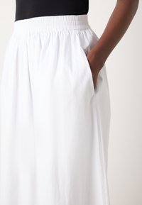 Jupe blanche à taille élastique avec poches latérales, au design fluide et à la texture douce. Le tissu tombe doucement sur la peau.