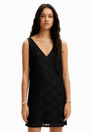 Vestido de encaje negro con escote en V, diseño sin mangas, que presenta patrones florales y un acabado texturizado. Acento de collar y pulsera en forma de corazón plateado.