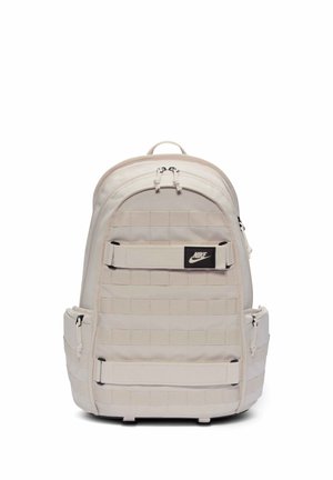 Hellbeiger Nike-Rucksack mit zwei vorderen Riemen, seitlichen Reißverschlusstaschen und einem oberen Griff, vor weißem Hintergrund gezeigt.