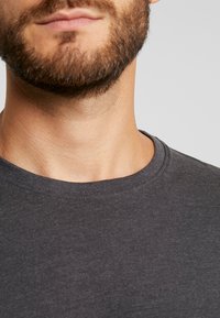 Mørkegrå bomull t-skjorte med rund hals. Stoffet har en jevn tekstur og er lett figursydd rundt kragen og skuldrene.