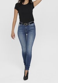 Mustat lyhythihaiset paidat yhdistettyinä tiukkoihin sinisiin farkkuihin ja mustaan vyöhön. Mallilla on päällään mustat korkokengät. Yksinkertainen, rento asu.