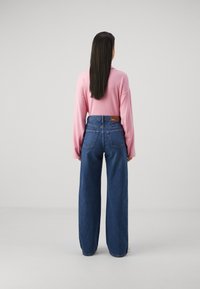 Light pink long-sleeve shirt paired with high-waisted, wide-leg blue denim jeans featuring back pockets and a branded leather patch.