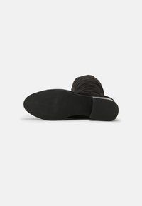 Black, knee-high boot with a slouchy design, soft suede texture, and a round toe. The sole is flat with a textured, rubber bottom.