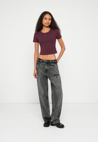 T-shirt de manga curta, corta, de cor borgonha com um logotipo subtil, combinada com jeans enegrecidos, desbotados e largos, e sapatos pretos.