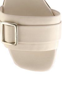Sandale beige à bout ouvert avec une large lanière sur le pied et une boucle argentée sur le côté.