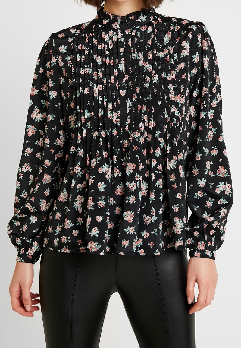 Blusa nera floreale con pieghe, caratterizzata da piccoli fiori rosa e verdi. Maniche lunghe con polsini elasticizzati, design a collo alto. Tessuto dalla texture liscia.