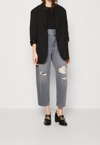 Blazer negro de gran tamaño, top negro, jeans grises de cintura alta y rotos, y tacones negros con detalles de cadena dorada. Conjunto simple y urbano.