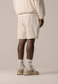 Cream-colored textured shorts and matching jacket, paired with beige New Balance sneakers and white socks featuring black lettering.