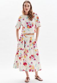 Ensemble floral en deux pièces comprenant un haut court à manches courtes et une longue jupe plissée. Tissu beige clair avec des motifs floraux vifs en rose, rouge et bleu.