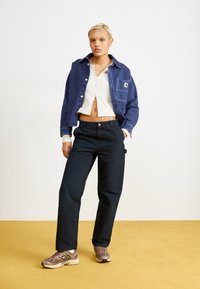Dunkelblaue Jeansjacke, gerippter weißer Cropped-Top, schwarze Hose und braune Sportschuhe. Einfaches Design, lässige Passform und unterschiedliche Texturen.