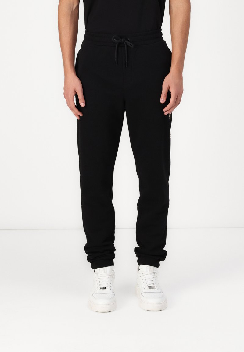 Schwarze Jogginghose mit einem Kordelzugbund, schmal zulaufenden Beinen und seitlichen Taschen. Kombiniert mit weißen Sneakers für einen Kontrast.