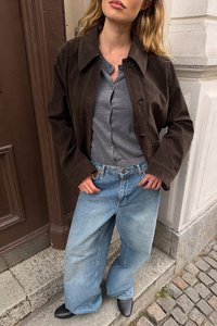 Tumepruun sametjope halli nööbitud särk üle, koos laia jalaga helesiniste teksade ja mustade teravatega kingadega, komplekt tänavamaa taustal.