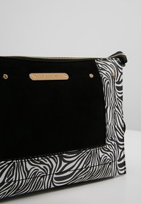 Pochette imprimé zèbre en noir et blanc avec un panneau avant en daim noir et une plaque logo River Island dorée ainsi qu'une fermeture éclair dorée.