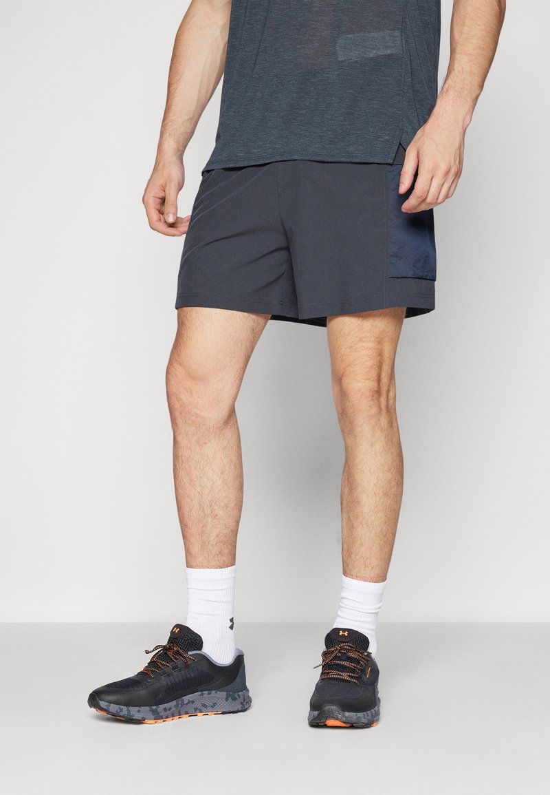 Herrernas träningsoutfit bestående av mörkgrå shorts med sidopanel, tillsammans med svarta sneakers och vita strumpor. Shorts har en slät yta.