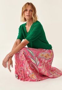 Top verde a maglia con maniche corte abbinato a una gonna rosa con un motivo floreale paisley e una texture fluida.