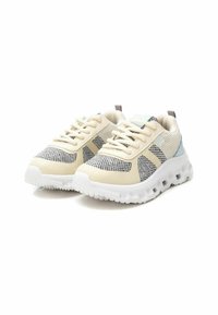 Zapatillas deportivas con una parte superior de malla crema, acentos grises, suela blanca texturizada y detalle en el talón de color azul claro. Incluye cordones y collar acolchado.