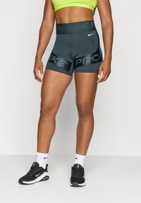 Szare spodenki sportowe z nadrukiem "NIKE PRO" na czarnym pasie. Wykonane z elastycznego materiału, uzupełnione czarnymi butami sportowymi i białymi skarpetkami.