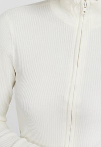 Valkoinen ribbed-tyylinen vetoketjullinen villapaita, jossa on korkea kaulus, tiukka istuvuus ja teksturoitu kangas. Vetoketjujuovi kulkee pystysuunnassa etupuolella.