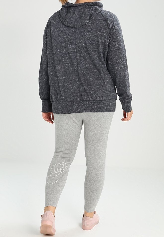 Donkere grijze hoodie met een capuchon en voorkeurszakken, gecombineerd met lichtgrijze leggings met een wit Nike-logo. Zachte, gestructureerde stof.