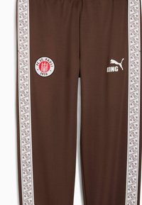 Brune sportsbukser med hvide mønstrede striber i siden, med et FC St. Pauli-logo og teksten "KING" i hvid på højre side.