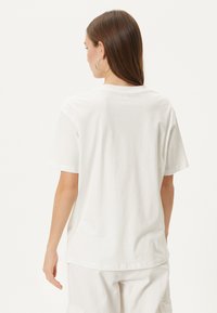 T-shirt en coton blanc à manches courtes, col rond et coupe décontractée. Texture lisse, sans motifs ni graphiques visibles.