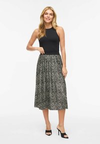 Czarny top bez rękawów zestawiony z długą, plisowaną spódnicą w czarno-kremowy wzór w jodełkę, do tego czarne sandały na obcasie z odkrytymi palcami.