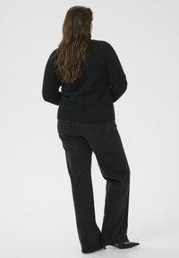 Pull en tricot noir et jeans en denim foncé. Le pull a un ourlet côtelé et des manches ajustées. Les jeans sont à coupe décontractée avec des poches arrière.