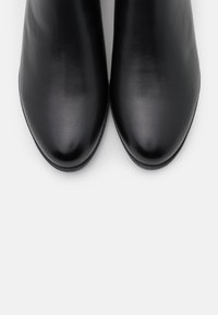 Botas de tobillo de cuero negro con una textura suave, punta afilada y diseño minimalista. Presentan un tacón bajo y un perfil esbelto.