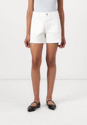 White denim shorts with a straight cut, featuring two back pockets, and a rolled hem. Matched with black flat shoes with decorative accents.