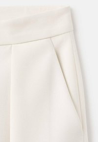 Pantaloni bianchi plissettati caratterizzati da una texture di tessuto liscia e una vita ampia, con linee diagonali visibili nel materiale.