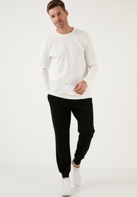 Weißes Langarmhemd mit strukturiertem Muster, kombiniert mit schwarzen tapered Hosen und weißen Sneakern. Einfaches, lässiges Design.