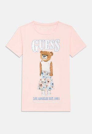 Pink t-shirt featuring a graphic of a bear in a floral dress, with "GUESS" printed above and "LOS ANGELES EST. 1981" below in blue lettering.