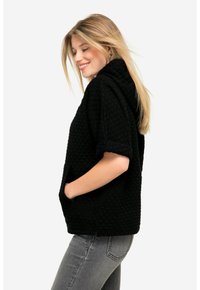 Giacca nera imbottita con zip e maniche corte, dotata di cappuccio e tasche frontali. Superficie strutturata con un motivo geometrico.