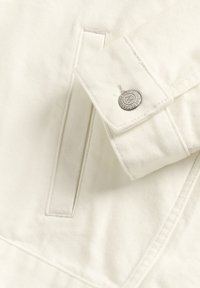 Jachetă din denim alb, cu un buzunar pe piept, nasture din metalargintat și detalii de cusătură vizibile pe mansete și pe corp.