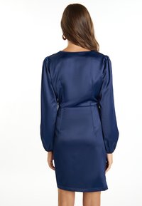Rochie elegantă de culoare bleumarin, confecționată din satin, cu mâneci lungi bufante, talie ajustată și decolteu clasic. Textură netedă pe toată suprafața.