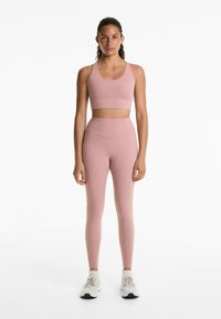 Roze sport-bh met bijpassende high-waisted leggings, gladde textuur, eenvoudig ontwerp en subtiele stiksels; gecombineerd met witte sneakers.