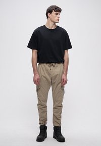 Juoda medvilninė trumpomis rankovėmis marškinėliai, derinami su smėlio spalvos kelnėmis su kišenėmis šonuose ir juodais auliniais batais. Lygus audinys, kasdienis stilius.