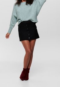 Helles blaues strukturiertes Sweatshirt mit lockerer Passform, kombiniert mit einem schwarzen Minirock mit Knöpfen auf der Vorderseite und bordeauxfarbenen, hohen Stiefeletten.