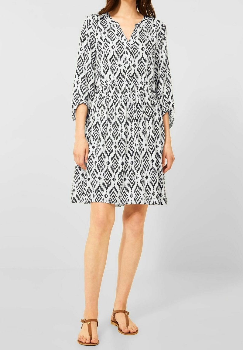 Robe à motifs noir et blanc, longueur genou, avec un décolleté en V et des manches trois-quarts. Tissu léger avec un détail de taille froncée.