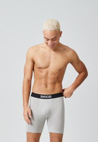Boxer aderenti grigi con un elastico nero che presenta la scritta "SNOCKS" in bianco. Il tessuto sembra morbido, con una texture liscia e un design aderente.
