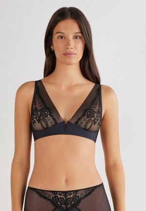 Zwarte kanten bralette met doorzichtige panelen en een diepe V-hals, met een kanten bloemenpatroon en een klein uitsnijdetail in het midden.