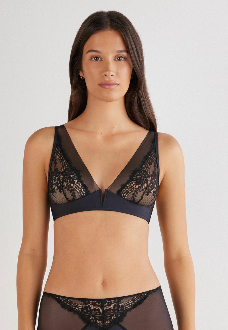 Zwarte kanten bralette met doorzichtige panelen en een diepe V-hals, met een kanten bloemenpatroon en een klein uitsnijdetail in het midden.