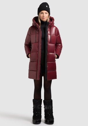 Burgundy puffer coat with a hood, glossy finish, quilted design, and zippered pockets, paired with black insulated snow boots.
