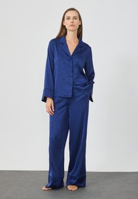 Set di pigiami in satin blu navy composto da una camicia con botttoni e pantaloni larghi, caratterizzato da un delicato motivo di stelle e lune, maniche lunghe e polsini ampi.
