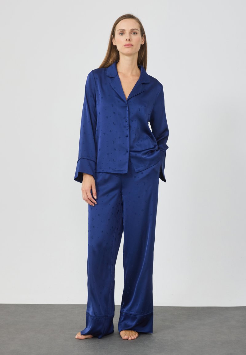 Set di pigiami in satin blu navy composto da una camicia con botttoni e pantaloni larghi, caratterizzato da un delicato motivo di stelle e lune, maniche lunghe e polsini ampi.