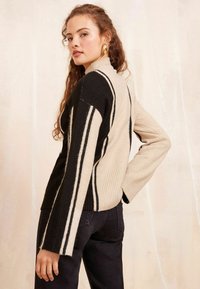 Maglione a righe con collo alto, caratterizzato da colori nero e crema, texture a costine e maniche lunghe con righe a contrasto.