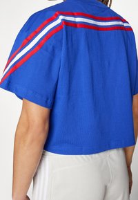 Blue short-sleeve crop top in cotton with red and white striped accents across the shoulders. Smooth texture, relaxed fit.