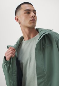 Zaļš viegls jaka ar rāvējslēdzēju priekšpusē un kapuci, ar elastīgām piedurknēm un teksturētu iekšpusi. Uz krūtīm ir izšūta logo.