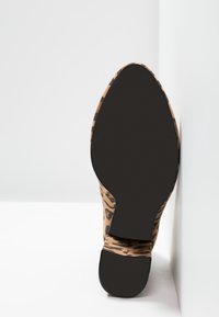 Chaussure à talon imprimé léopard avec une tige lisse couleur tan et des détails noirs. Présente un bout arrondi et une semelle en caoutchouc noire texturée.